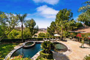 Backyard pool with rock waterfall, lush landscaping, and ivy-covered patio at the West Valley Estate in West Hills.
