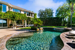 Backyard pool with rock waterfall, lush landscaping, and ivy-covered patio at the West Valley Estate in West Hills.