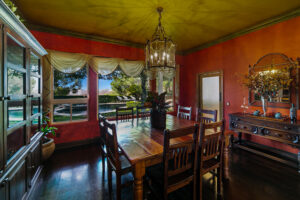 Formal dining room at West Valley Estate with red walls, chandelier lighting, wood furniture, and windows overlooking pool and hillside.