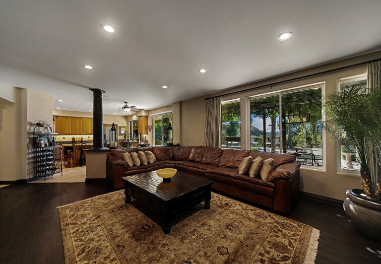 Spacious family room at West Valley Estate featuring a leather sectional, wood floors, and open kitchen concept with canyon views.