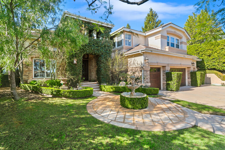 Front exterior of the West Valley Estate in West Hills featuring lush landscaping, ivy-covered stone entry with fountain, and a 4-car garage.