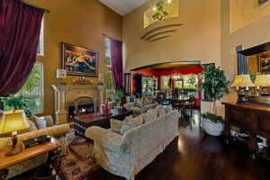 Formal living room at the West Valley Estate with vaulted ceilings, fireplace, floor-to-ceiling drapes, and open flow to the dining area.