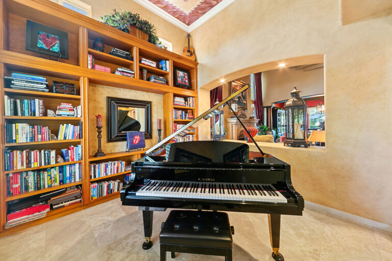 Grand piano and custom bookshelf library in the music room of the West Valley Estate, with open archway revealing adjacent living areas and elegant decor.