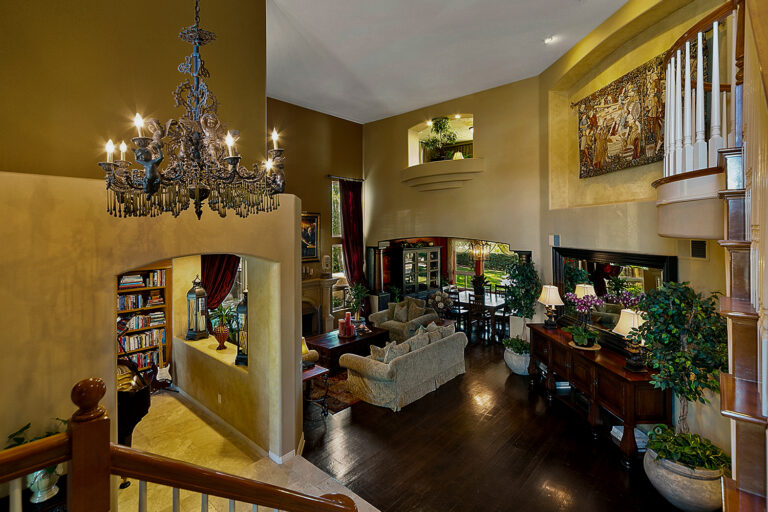 Formal living room at the West Valley Estate with vaulted ceilings, fireplace, floor-to-ceiling drapes, and open flow to the dining area.