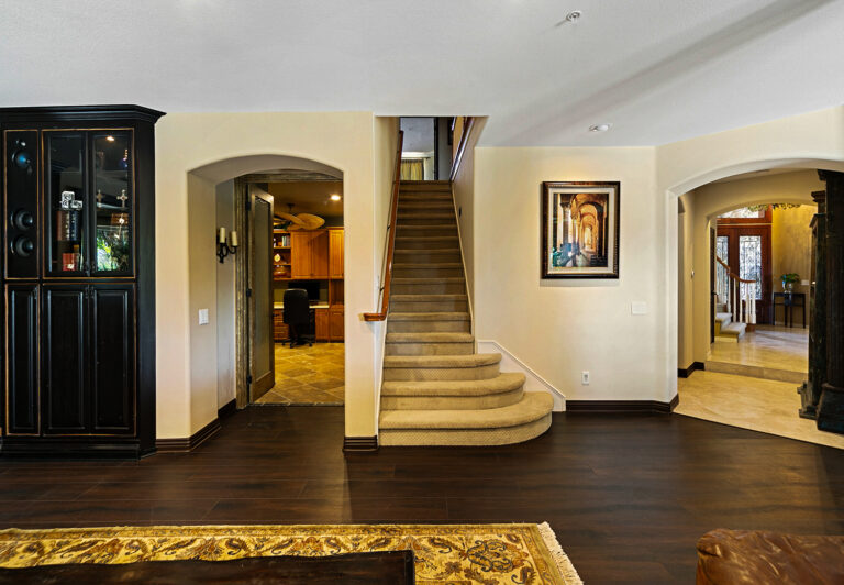 Ground-level view at West Valley Estate showing second staircase, office entry, and connected living spaces with hardwood floors and limestone.